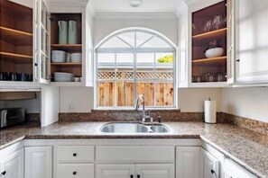 A kitchen with white cabinets, a granite countertop, a double sink, and a window with a view of a wooden fence.