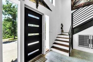 Eine moderne Treppe mit weißen Stufen und schwarzen Geländern, die zu einer schwarzen Tür mit Glasfeldern führt.