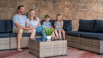 A family on a dark-colored sofa with a woven coffee table in front, set against a stone wall.