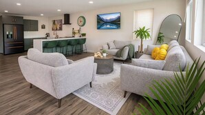 A modern living room with grey sofas, a coffee table, and a kitchen area with green bar stools. - 2 Waterfront Houses |Jacuzzi |Dock For Boat|Groups (New Haven)