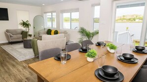 A modern living room with a dining area, large windows, and a view of a body of water. - 2 Waterfront Houses |Jacuzzi |Dock For Boat|Groups (New Haven)