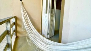 A hammock in a hallway with a wooden railing and a door in the background. - Mother Africa Apartment – ​​5 minutes from Primeira Praia (First Beach) (Morro de São Paulo)