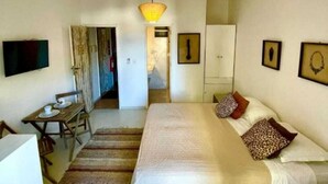 A bedroom with a bed, a desk, a chair, a television, and a wardrobe. - Mother Africa Apartment – ​​5 minutes from Primeira Praia (First Beach) (Morro de São Paulo)