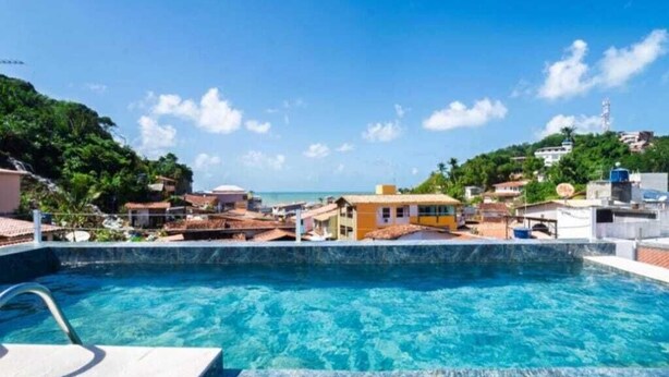 A clear blue pool with a view of a coastal town, surrounded by buildings and greenery. - Mother Africa Apartment – ​​5 minutes from Primeira Praia (First Beach) (Morro de São Paulo)