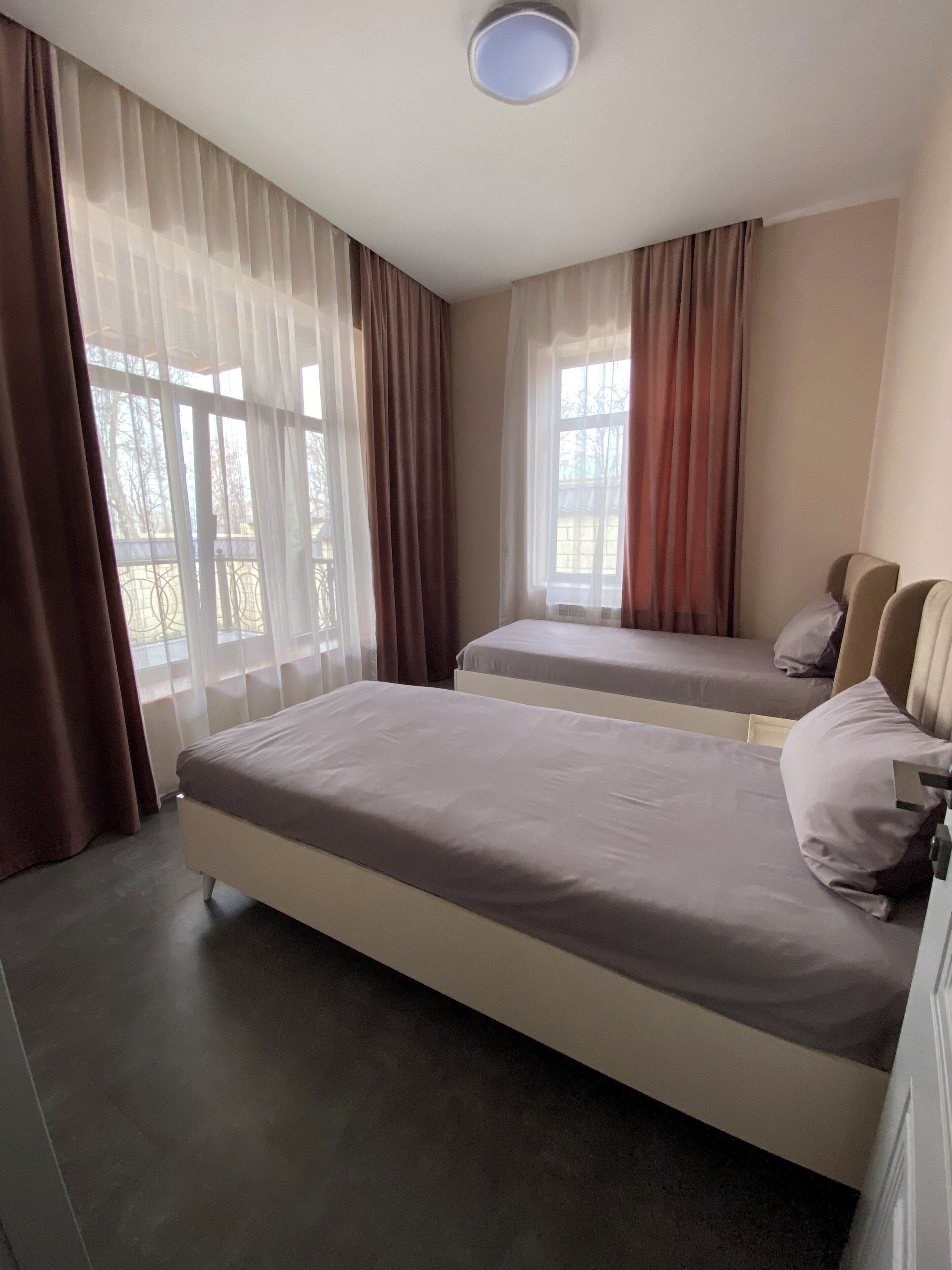 Habitación de hotel con dos camas, una lámpara en el techo y ventanas grandes con cortinas.