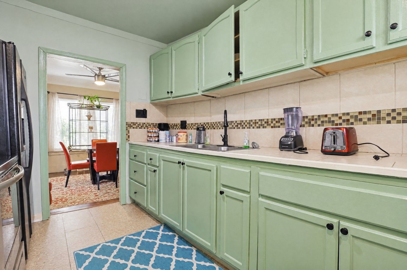 A kitchen with green cabinets, a countertop, a sink, a blender, and a toaster.