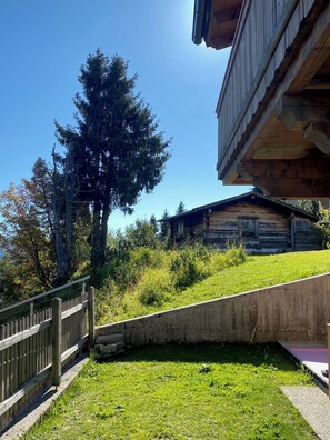 Une cabane en bois avec un toit en pente, entourée d’une zone herbeuse et d’arbres.
