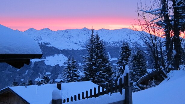 A snowy mountain landscape with a wooden fence and snow-covered buildings.