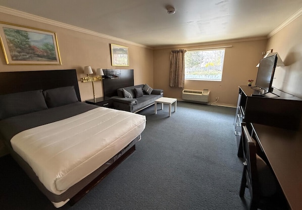 A hotel room with a bed, a sofa, a desk, a television, and a window with curtains. - Kiteville Phoenixville (Phoenixville)