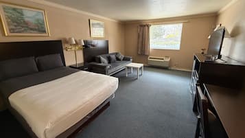 A hotel room with a large bed, a sofa, a desk, a television, and a window with curtains.