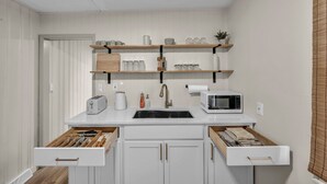A kitchen with white cabinets, a black sink, a microwave, and shelves above the counter. - Bright 2BR w/ Sunroom Near Downtown & Beach (Euclid)