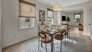 A dining area with a table set for four, surrounded by chairs, with a large window and a hanging light fixture. - Bright 2BR w/ Sunroom Near Downtown & Beach (Euclid)