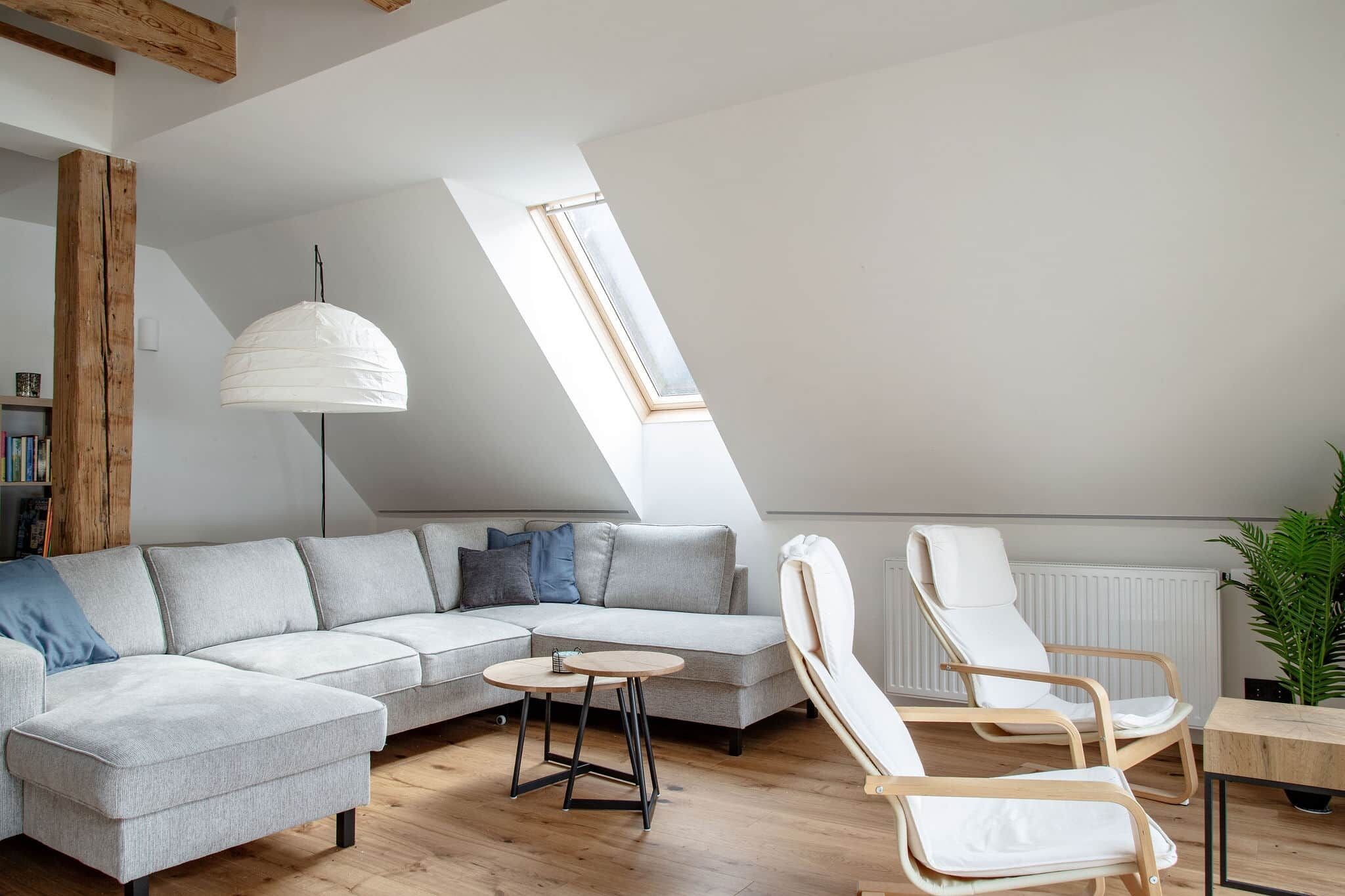 Ein modernes Schlafzimmer im Loft-Stil mit schrägen Wänden, einem großen Fenster, einer Couch, einem Esstisch und einem Stuhl.