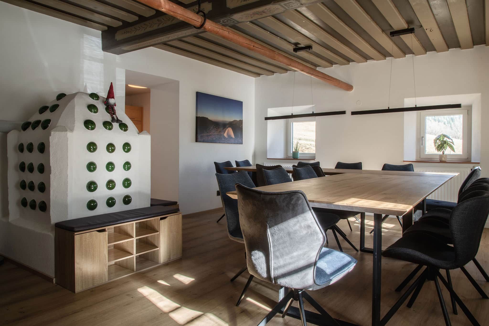 Ein moderner Essbereich mit einem Holztisch, schwarzen Stühlen, einer weißen Wand mit grünem Mosaik und einem Landschaftsbild.