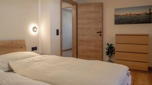 A bedroom with a wooden bed, a nightstand, a wall-mounted light, a door, a dresser, and a small plant. - Detox Almhaus - chalet in a unique, secluded location (Pusterwald)