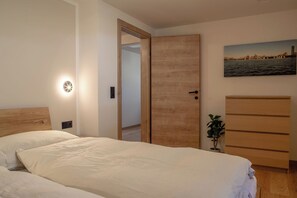 A bedroom with a wooden bed, a nightstand, a wall-mounted light, a door, a dresser, and a small plant. - Detox Almhaus - chalet in a unique, secluded location (Pusterwald)