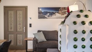 Une pièce comprenant un canapé, une petite table, une porte ornée de motifs floraux et un tableau représentant un paysage montagneux, accroché au mur.