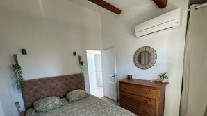 Un dormitorio con cama, cómoda de madera, unidad de aire acondicionado, espejo y puerta que da a otra habitación.