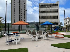 Terrasse extérieure avec parasols, aire de jeux et immeubles de grande hauteur en arrière-plan.