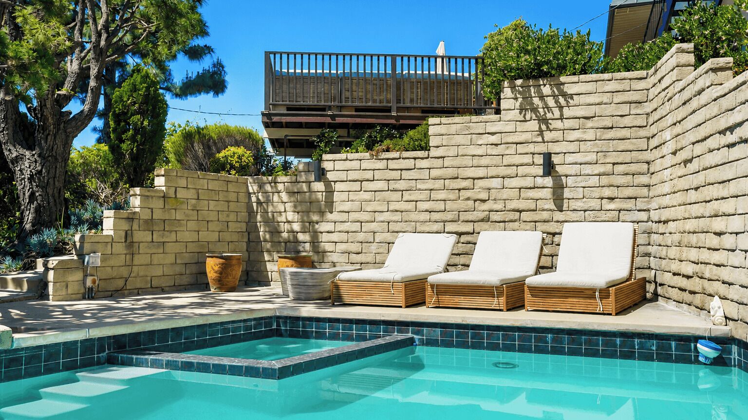 A pool area with a brick wall, three lounge chairs, and a small pool.