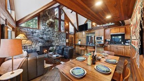 A cozy cabin interior with a stone fireplace, wooden dining area, and a stone wall. - Grand Elk Chalet by Avantstay Private Beach + Pier + Hot Tub Historic A-frame in Carnelian Bay Near Tahoe City + Hiking Trails (Carnelian Bay)