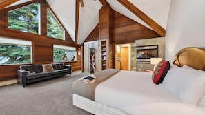 A bedroom with a large bed, a black leather sofa, wooden beams, and a fireplace. - Grand Elk Chalet by Avantstay Private Beach + Pier + Hot Tub Historic A-frame in Carnelian Bay Near Tahoe City + Hiking Trails (Carnelian Bay)