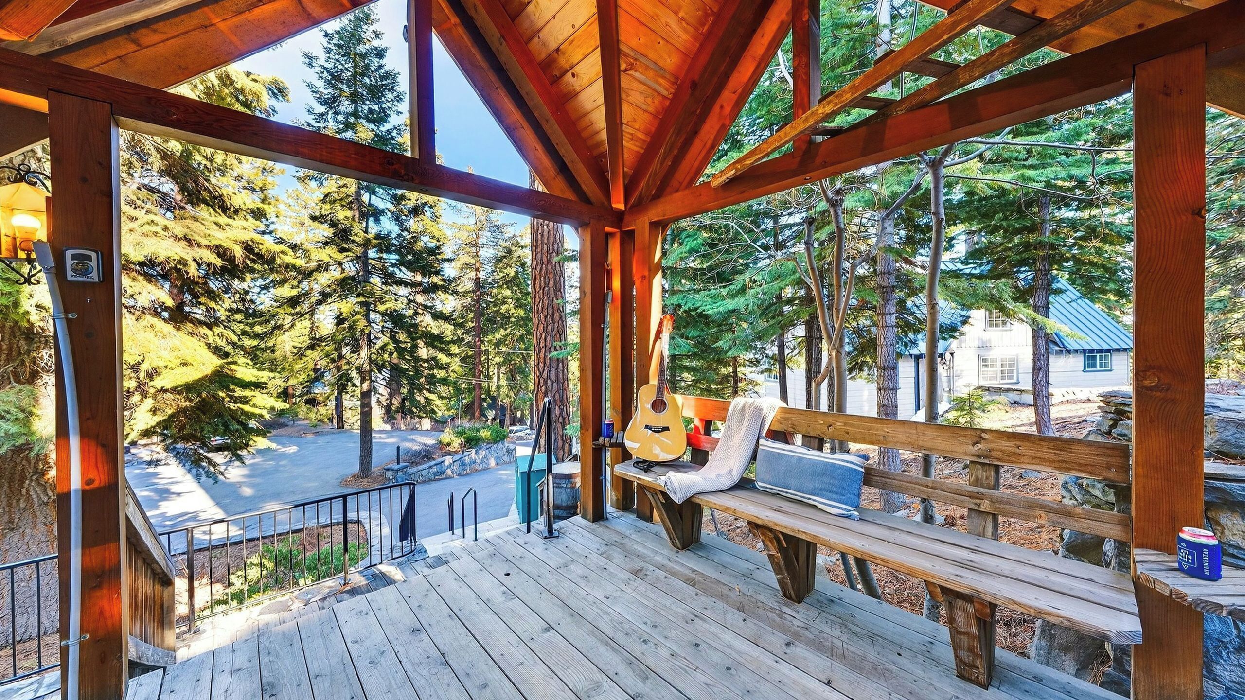Eine Holzterrasse mit einer Bank und einer Gitarre, mit Blick auf ein bewaldetes Gebiet.