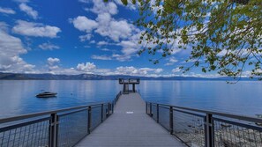 A wooden pier leading to a dock with a boat, surrounded by calm water and mountains. - Grand Elk Chalet by Avantstay Private Beach + Pier + Hot Tub Historic A-frame in Carnelian Bay Near Tahoe City + Hiking Trails (Carnelian Bay)
