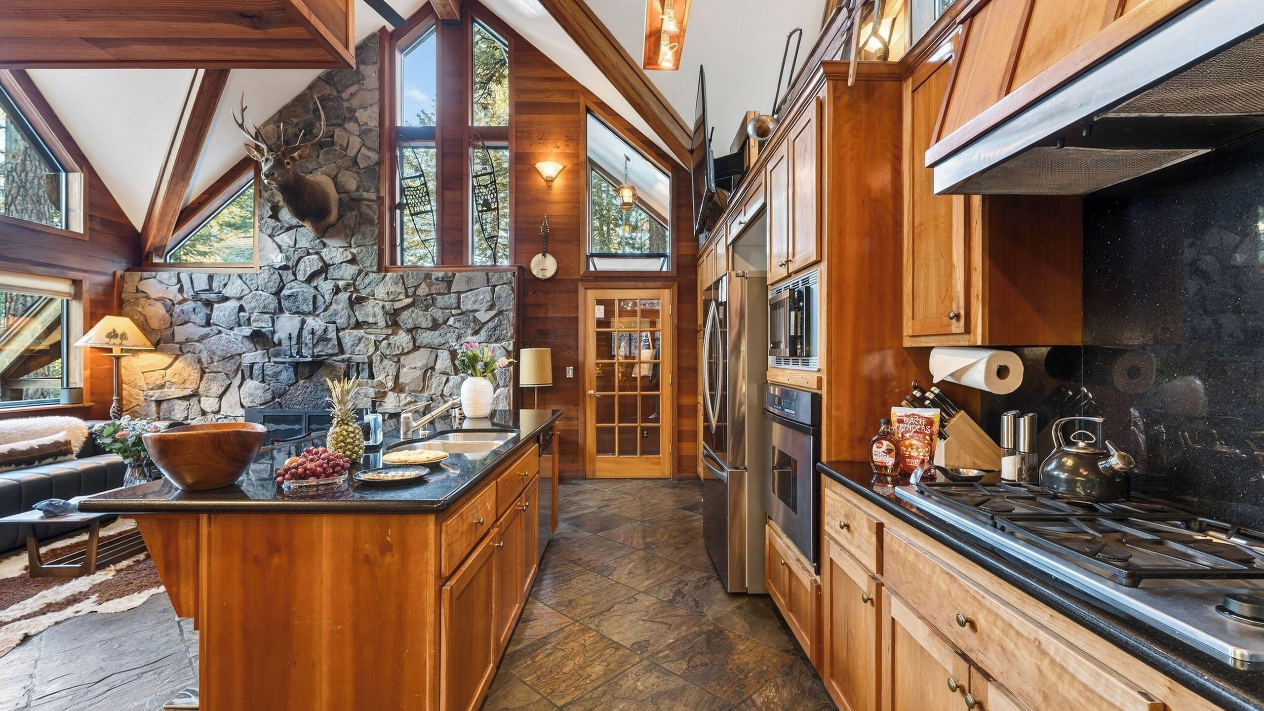 A kitchen with wooden cabinets, a stone wall, and a large island with fruit and a bowl.