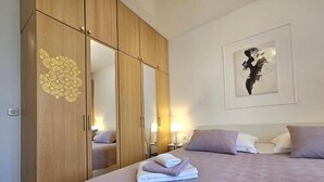 Ein Hotelzimmer mit Bett, Schrank, einem Gemälde und einem Nachttisch mit Lampe.