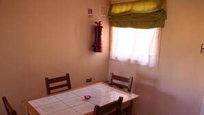 Un comedor con una mesa, sillas, un extintor y una ventana con cortinas.
