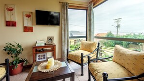 Habitación con sofá, una mesa con vela, televisión y ventana con vista a zonas verdes.
