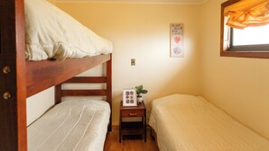 Una habitación pequeña y acogedora con literas, una mesita de noche con una planta y un cuadro en la pared.