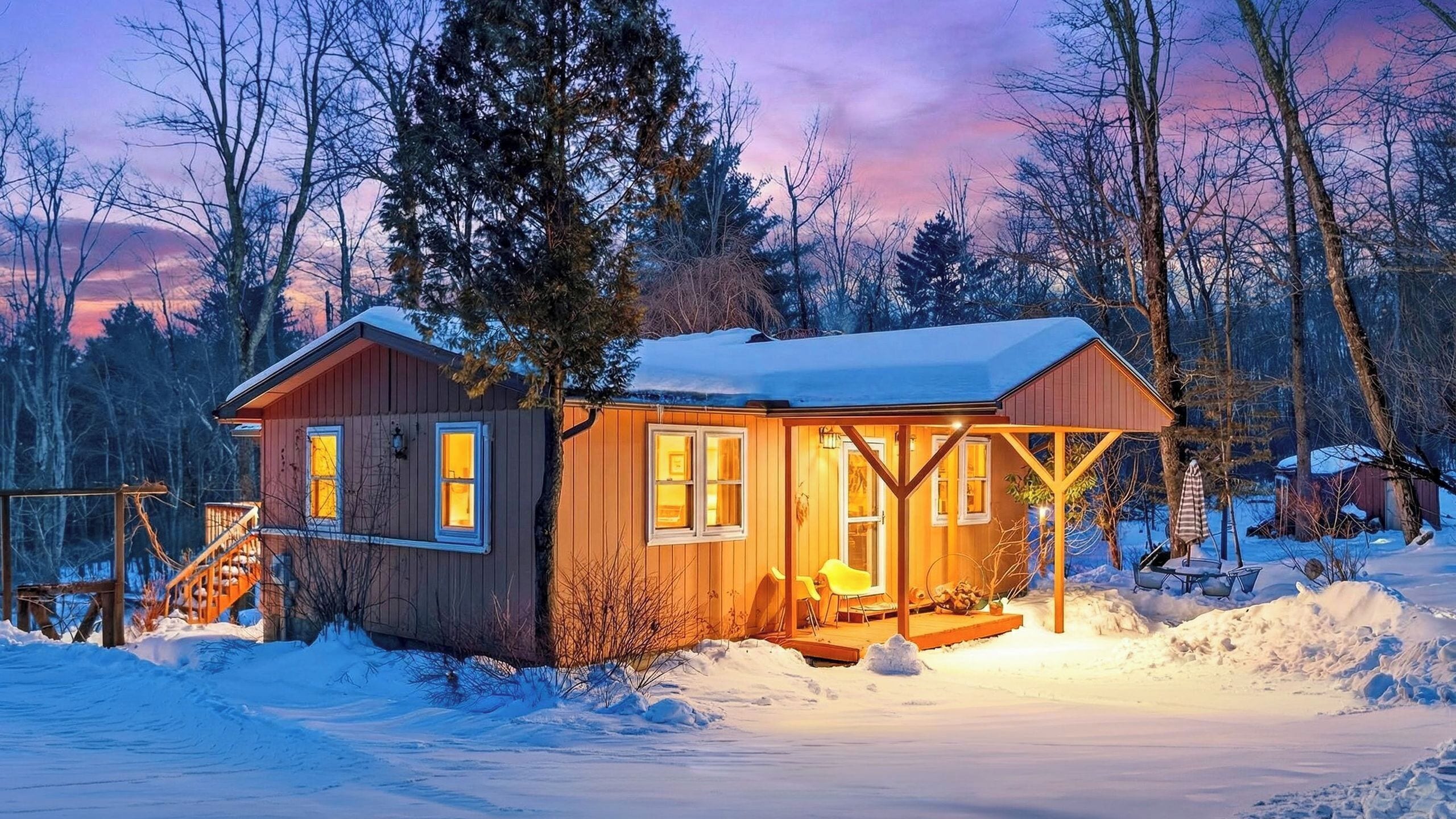 Une cabane en bois dotée d’un porche, entourée de neige et d’arbres.