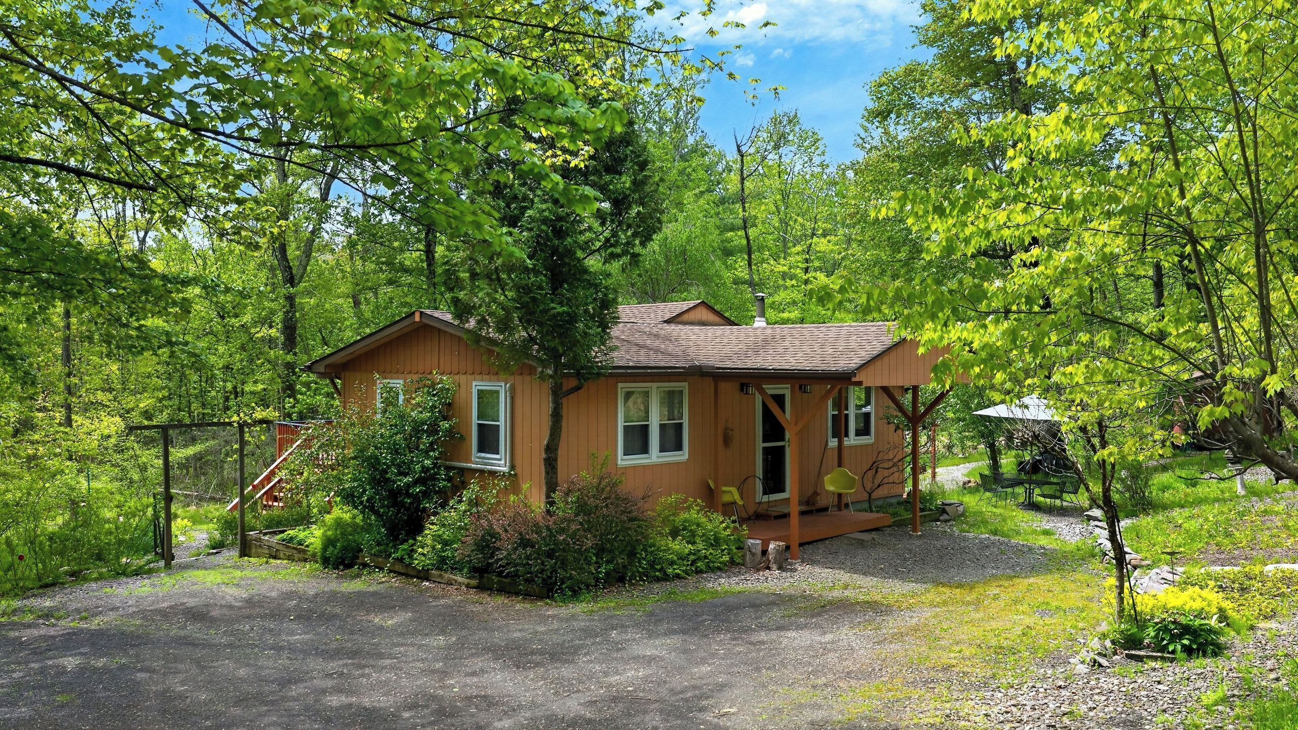A small wooden cabin with a porch, surrounded by dense green foliage.