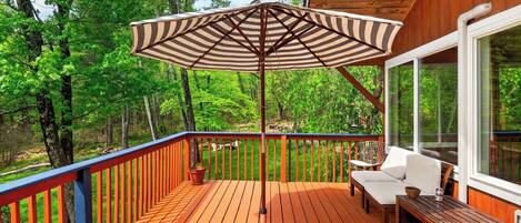 A wooden deck with a striped umbrella, outdoor seating, and a view of a forest.