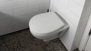Ein kleines Badezimmer mit weißen Fliesen, einer weißen Toilette und einem Wand-Spülknopf.