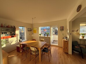 A dining area with a wooden table and chairs, a kitchen with shelves and a radiator, and a view through a window. - Fantastic 1 bedroom apartment in downtown Reykjavík (Reykjavík)