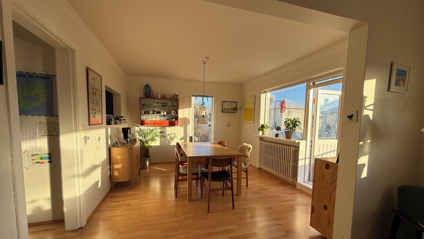Ein Essbereich mit Holztisch und -stühlen, einem Heizkörper und einem Fenster mit Pflanzen.