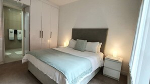 Une chambre à coucher comprenant un lit, des tables de chevet, une armoire et une porte vitrée donnant sur une salle de bain.
