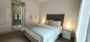 Une chambre à coucher comprenant un lit, des tables de chevet, une armoire et une porte vitrée donnant sur une salle de bain.