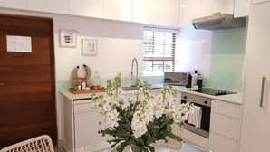 Une cuisine moderne avec des meubles blancs, une hotte en acier inoxydable, une table à manger en verre et un vase rempli de fleurs blanches.