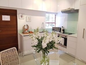 Une cuisine moderne avec des meubles blancs, une hotte en acier inoxydable, une table Ă manger en verre et un vase rempli de fleurs blanches.