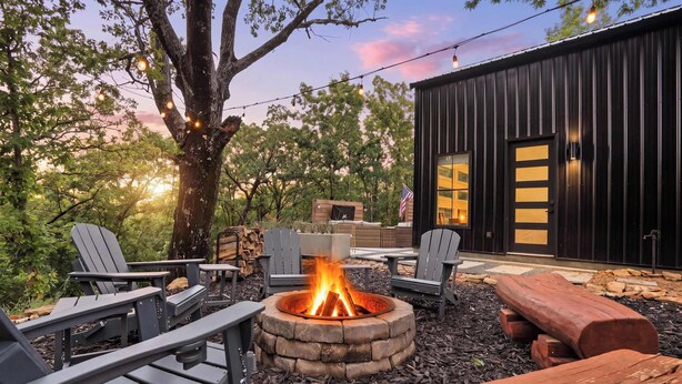 Un foyer entouré de fauteuils Adirondack, une terrasse en bois et un bâtiment moderne doté d’une grande fenêtre.