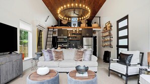 Un salon moderne avec un plafond haut, un grand lustre, un canapé, une table basse et un téléviseur.