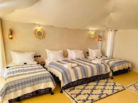 A room with four beds, each with patterned bedding, a yellow carpet, and wall-mounted lights.