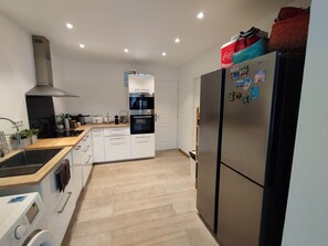 A modern kitchen with a built-in oven, a stainless steel refrigerator, and a washing machine. - Beach house: terrace, relaxation, air conditioning, wifi (Hyères)