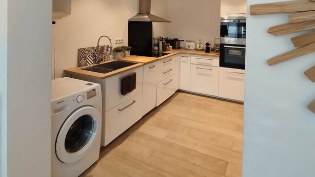 A modern kitchen with white cabinetry, a built-in washing machine, and a wooden countertop. - Beach house: terrace, relaxation, air conditioning, wifi (Hyères)