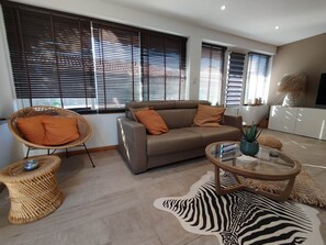 A living room with a sofa, a wicker chair, a glass coffee table, and a zebra-patterned rug. - Beach house: terrace, relaxation, air conditioning, wifi (Hyères)