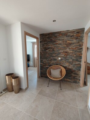 A room with a stone wall, a wicker chair, and a tiled floor. - Beach house: terrace, relaxation, air conditioning, wifi (Hyères)